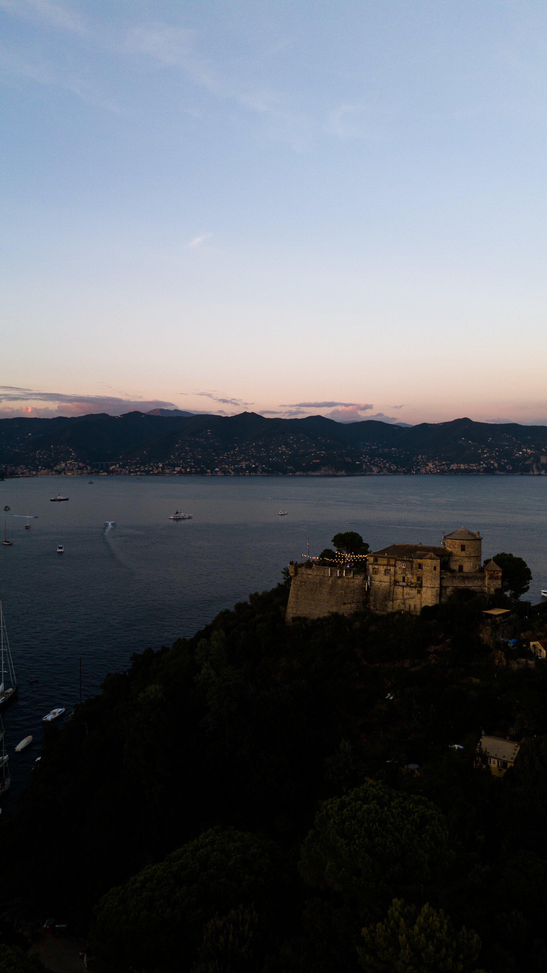Castello sulla scogliera al tramonto con luci, ripresa verticale drone evento serale